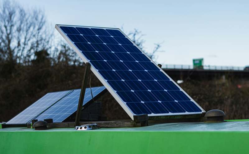 Person using a foldable portable solar panel in a mountain campsite with gear powered nearby