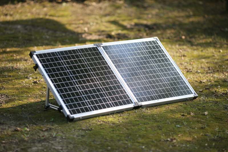 Two team members setting up a portable solar panel beside a camper van at sunrise